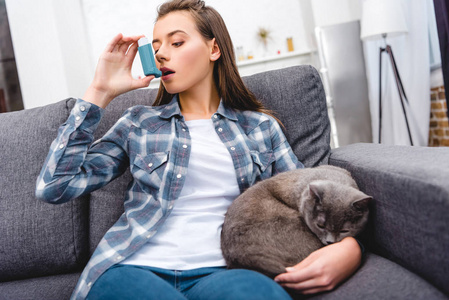 年轻女子在沙发上和猫坐在一起时使用吸入器