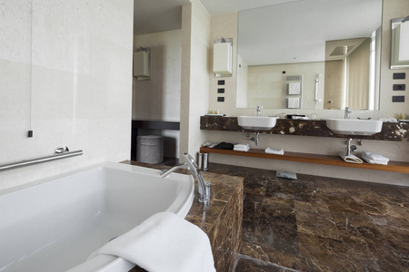 现代浴室内部有双水槽和大镜子，浴缸，瓷砖，窗户和毛巾。