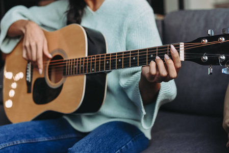 穿着绿松石毛衣在家沙发上弹吉他的混血女孩