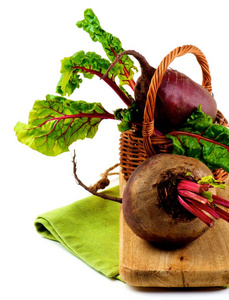 新鲜的生有机甜菜根，绿色甜菜顶部在柳条篮子上，在白色背景上的木板特写。