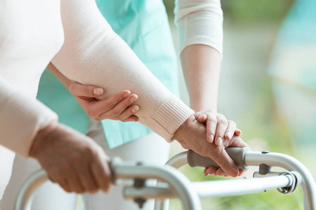 s hands holding a walker and helpful nurse supporting her