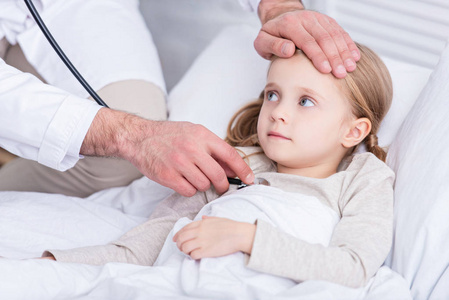 穿白色外套的儿科医生在家用听诊器检查生病的孩子的图像
