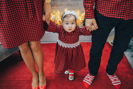 孩子在圣诞树灯的背景上穿红色西装, 牵着父母的手