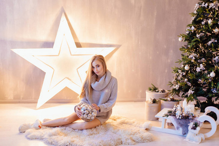 美丽的年轻女子坐在圣诞树下, 在节日内部盛满银球的碗