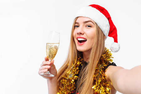 快乐的女人戴着圣诞老人的帽子，手里拿着一杯香槟，给自己拍照。