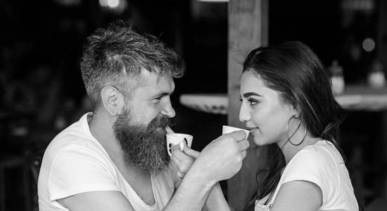 男人用胡子和迷人的微笑女孩喝咖啡。情侣相爱在咖啡馆喝黑咖啡咖啡。情侣在咖啡馆里过得开心。喝杯咖啡分享浪漫情怀