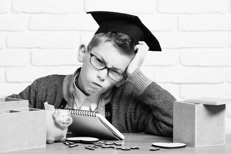 在灰色的毛衣和眼镜坐在办公桌前字木数字粉色小猪猪在与银行毕业帽在课堂上的背景墙上的白砖年轻可爱的学生男孩
