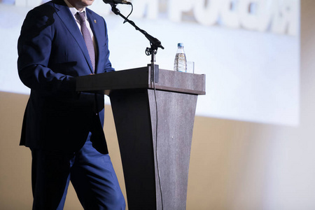 的后视图演讲者站在讲台后面模糊转身女孩拿着一本书在她的腿和马尾辫