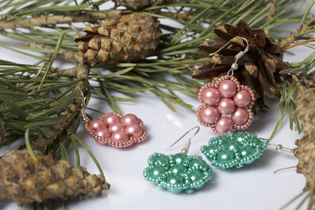 s earrings from beads among pine branches with cones. On a white