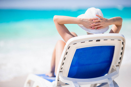 在热带海滩上的躺椅上戴帽子的年轻妇女