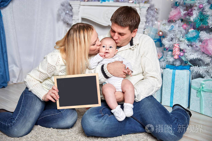幸福的家庭拿着一张空白的圣诞卡, 坐在舒适的客厅里的地毯上