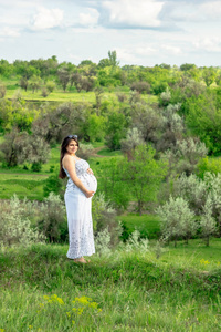 穿着白色衣服的孕妇在夏天的一片开花草地上休息