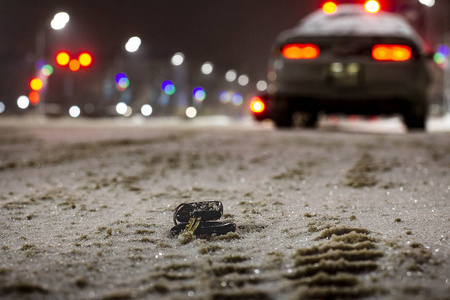 路上丢失的汽车钥匙在夜间的第一场雪中粉状。 模糊背景