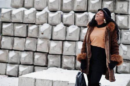 穿着羊皮外套和帽子的非裔美国妇女在冬日的雪石背景下摆好姿势。