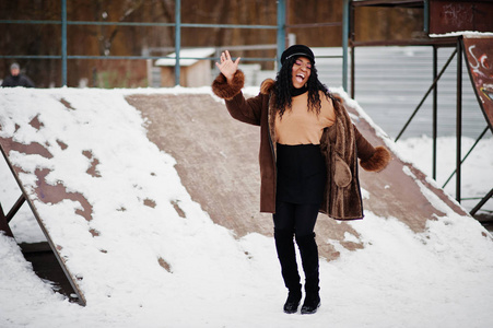 穿着羊皮外套和帽子的非裔美国妇女在冬日的雪地背景下摆好姿势。