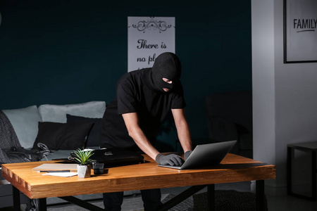 男性小偷在室内使用笔记本电脑照片