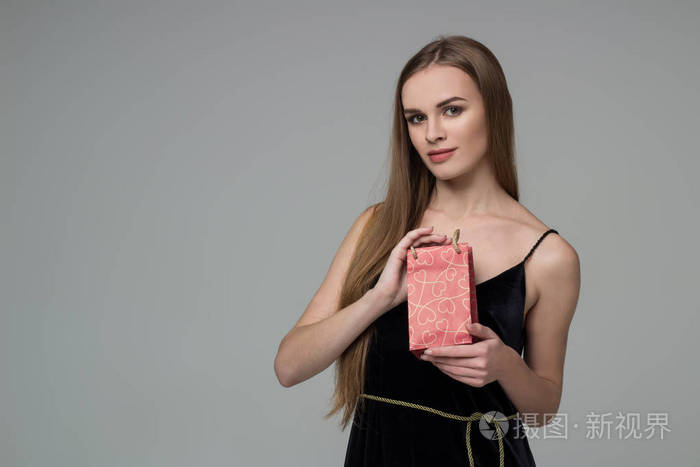 年轻的模特长头发的金发女孩穿着黑色的手拿红纸礼物包