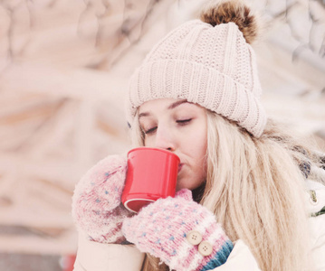 微笑美丽的年轻女人在户外喝热可可。 下雪的天气。 寒假。