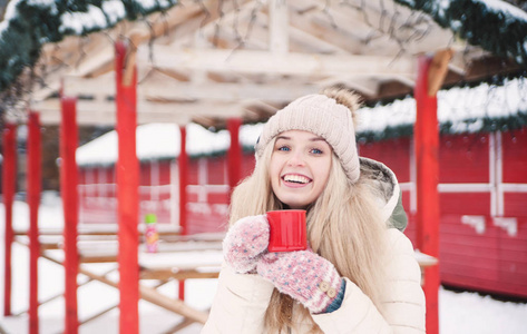 微笑美丽的年轻女人在户外喝热可可。 下雪的天气。 寒假。