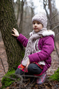 小女孩坐在秋天森林里的一棵树附近。