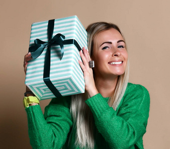 一个漂亮的微笑的金发女孩拿着礼品盒和看着它的肖像, 孤立在颜色米色的背景