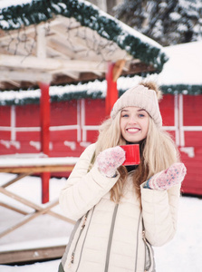 微笑美丽的年轻女人在户外喝热可可。 下雪的天气。 寒假。