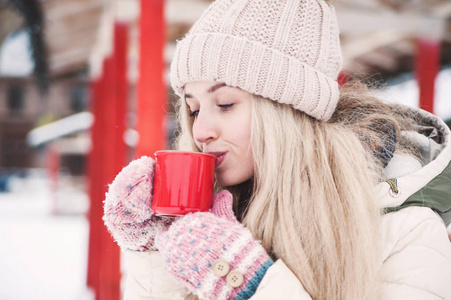 微笑美丽的年轻女人在户外喝热可可。 下雪的天气。 寒假。