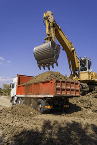 施工现场黄色挖掘机将土装入红色自卸汽车车身.照片