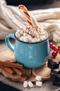 一杯热巧克力，上面有棉花糖和一根棒棒糖棒在针织毛毯背景上。 舒适温暖的冬季乡村构图