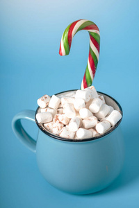 一杯热巧克力，上面有棉花糖，在蓝色背景上贴上棒棒糖。 舒适温暖的冬卡