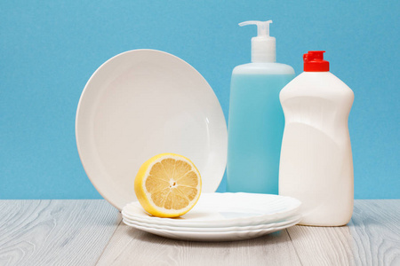 塑料瓶的洗碗液，玻璃和瓷砖清洁剂，清洁板和柠檬在蓝色背景。 洗涤和清洁的概念。