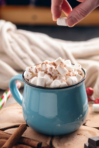 手把棉花糖扔在一杯热巧克力的木制背景上。 舒适温暖的冬季乡村构图