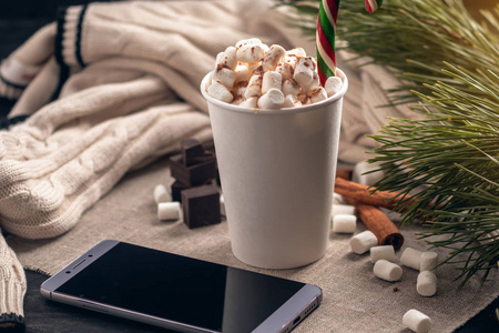 一杯热巧克力，上面有棉花糖，在巧克力和肉桂的背景上有一根棒棒糖棒。 一个舒适的圣诞家庭假日的概念