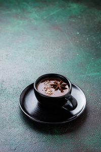 热巧克力与八角和坚果在黑色陶瓷杯在旧的深绿色混凝土背景。 选择性聚焦。