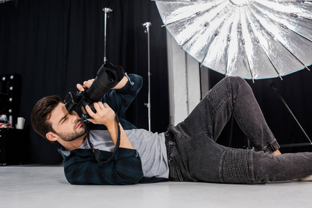 英俊的年轻摄影师躺在摄影棚里用摄影摄像