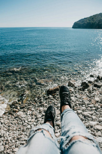 女孩在时尚撕破的牛仔裤和运动鞋坐在海滩上休息