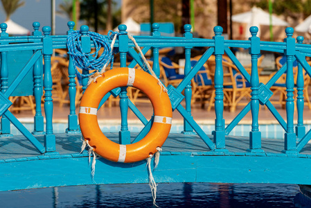 橙色和白色救生圈，绳子挂在游泳池上方的小木桥上