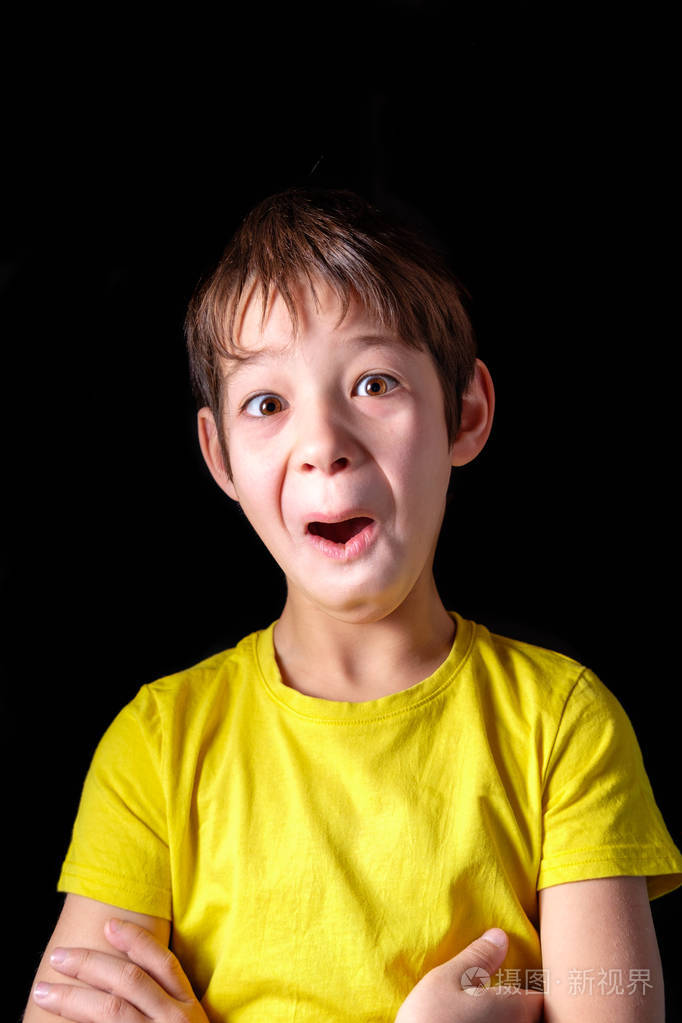 穿黄色t恤的男孩在黑色背景上做滑稽的表情