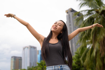 年轻美丽的亚洲妇女放松在公园与举起手臂