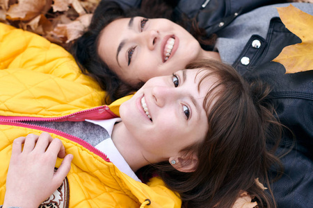 漂亮的女人和十几岁的女孩在秋天公园摆姿势。 他们躺在落叶上。 秋天的美丽景观。