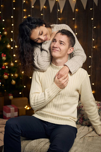 这对年轻夫妇穿着白色杉树的圣诞灯和装饰，穿着深色木制背景的寒假概念