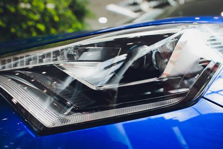 关闭镜头前大灯在豪华蓝色汽车背景。现代而昂贵的跑车概念