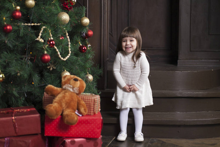小可爱的女孩和她的玩具熊在圣诞树附近。