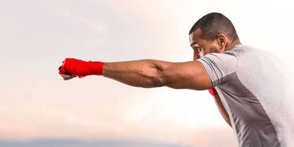 强壮的运动员，带着拳击磁带，在日落的背景下战斗