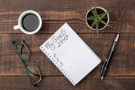 2019年的目标。文字在笔记本上，笔眼镜和咖啡在棕色的木制背景。