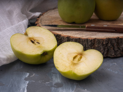 两个绿色的金色苹果和两个半在一个木盘和灰色背景棉白色餐巾菜刀。 快关门。
