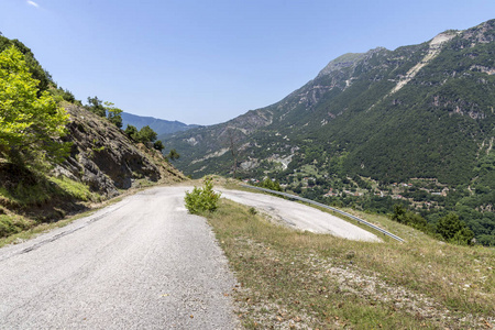 在阳光明媚的夏天，看到一条农村狭窄的道路，急转弯和山脉地区TzoumerkaEpirus希腊。