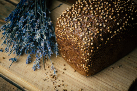 烘焙自制黑麦黑面包与香菜种子和薰衣草在乡村木桌背景。