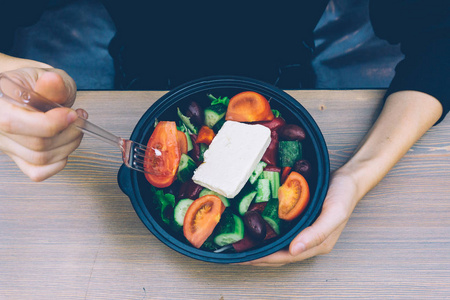 快餐希腊沙拉与新鲜蔬菜，Feta奶酪和橄榄木桌与女性的手。