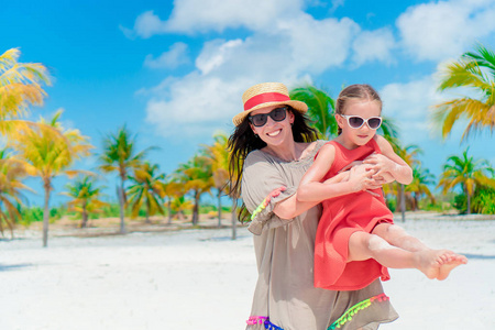 小小的可爱的女孩和年轻的母亲在地处热带的海滩